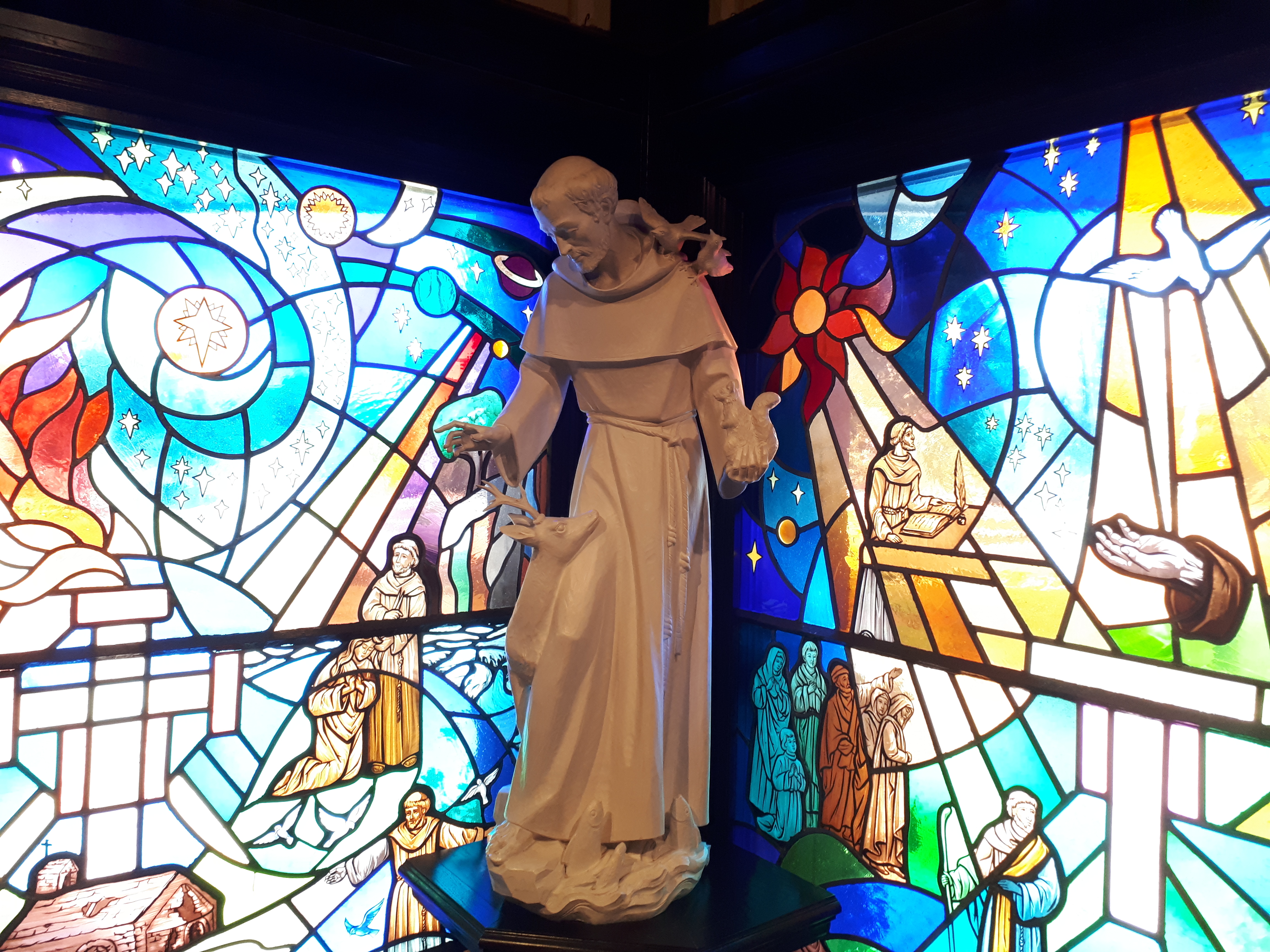 statue of St. Francis in front of stained glass windows